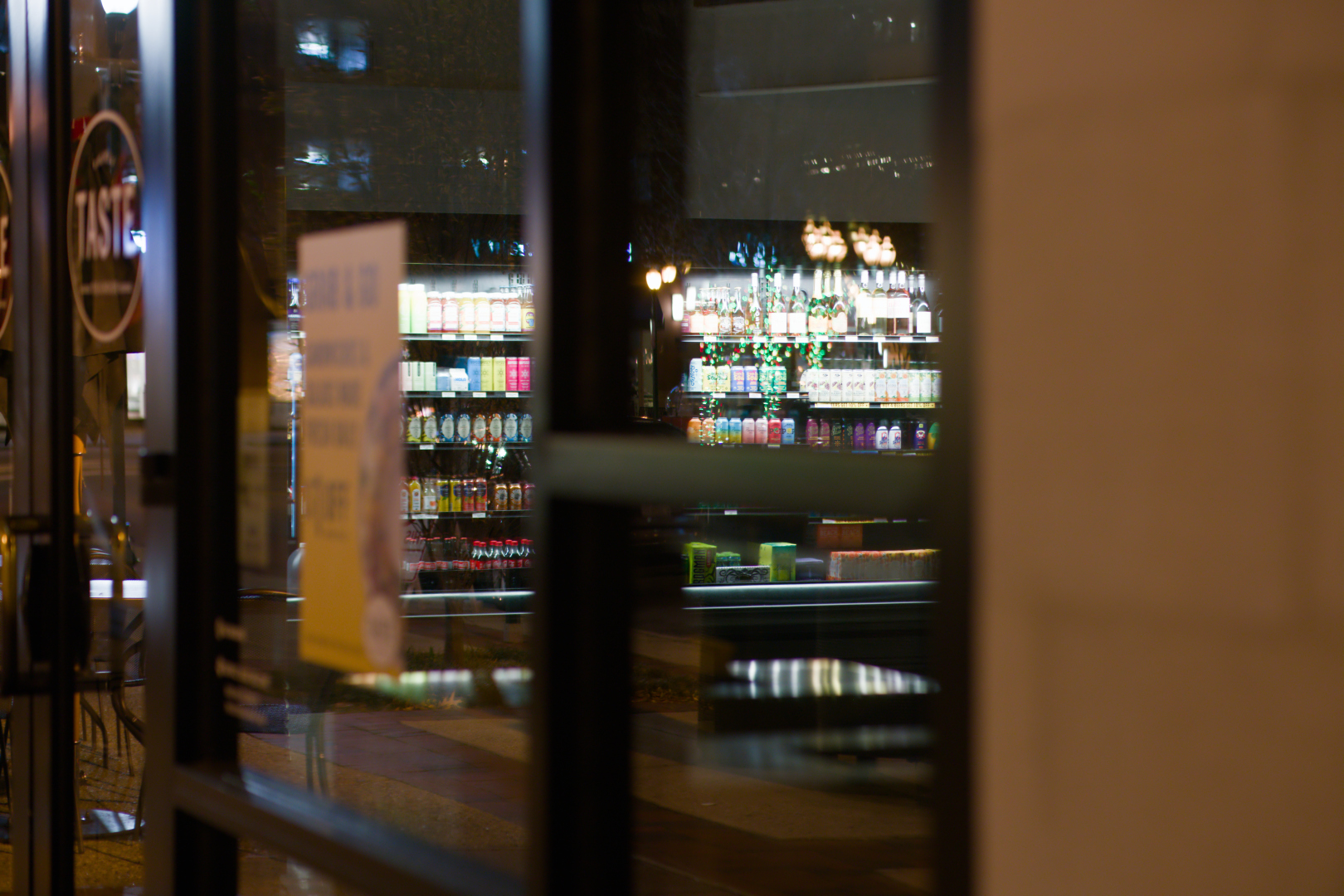 A nighttime shot of a food establishment. The business is closed for the night and the lights are off, but their beverage display coolers are brightly lit, exposing the rich colors of a variety of juice and soda products.
